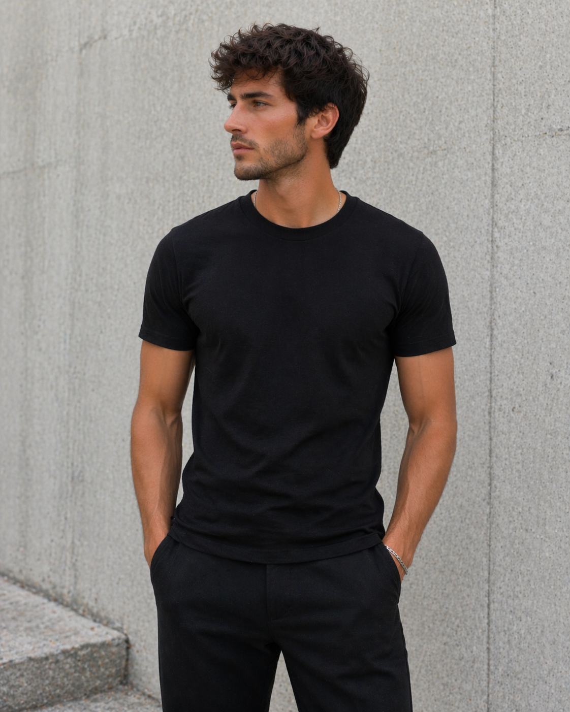 Man wearing a black t-shirt and pants against a gray concrete wall.