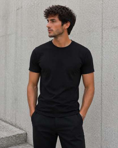 Man wearing a black t-shirt and pants against a gray concrete wall.