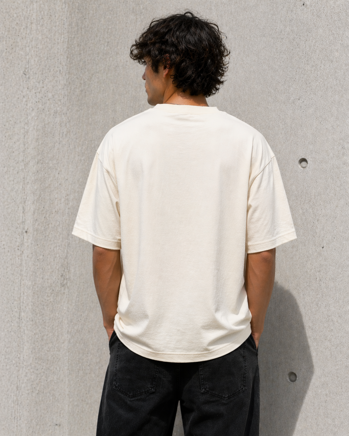 Person wearing a plain white t-shirt against a gray concrete wall