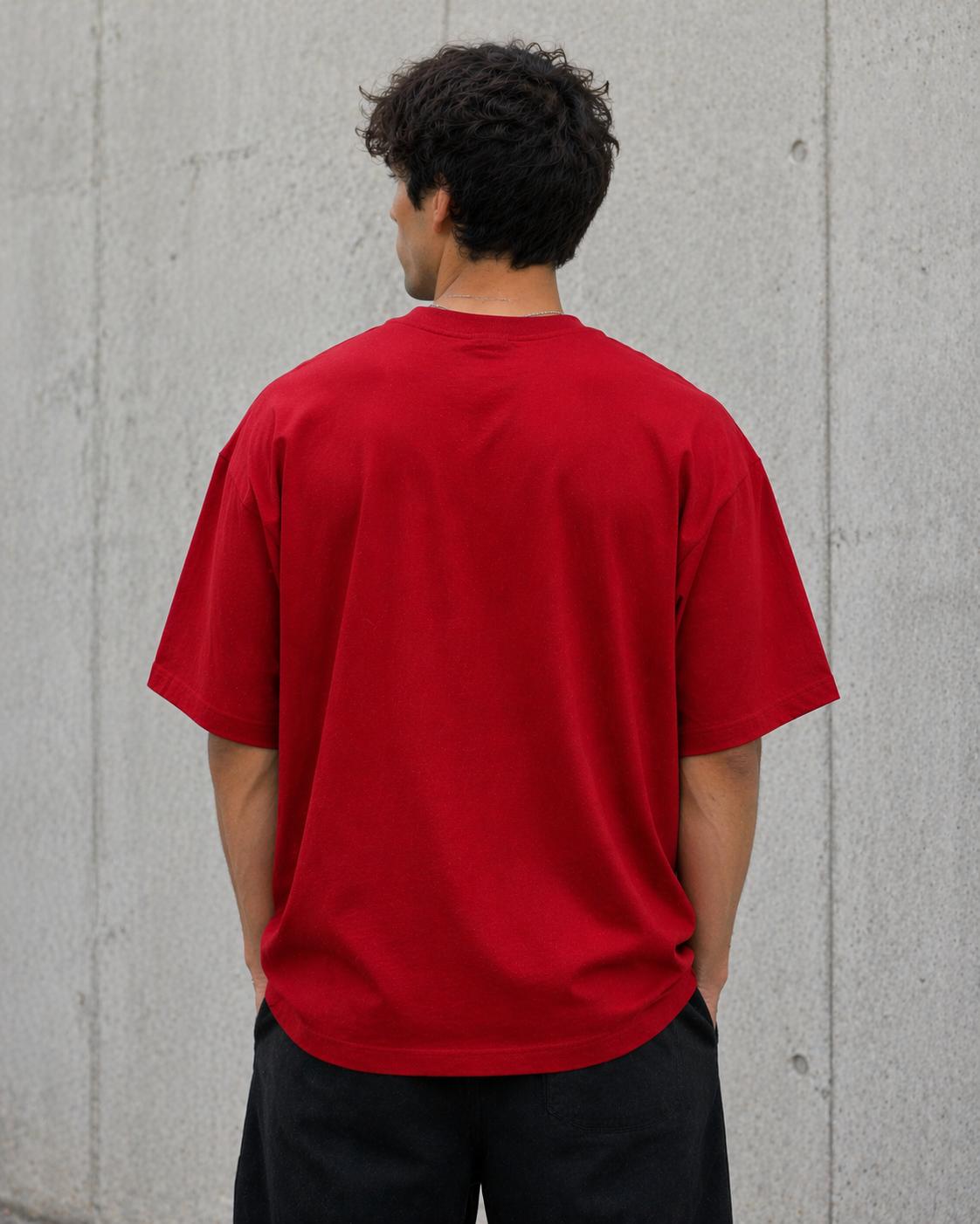 Person wearing a red t-shirt against a gray concrete wall