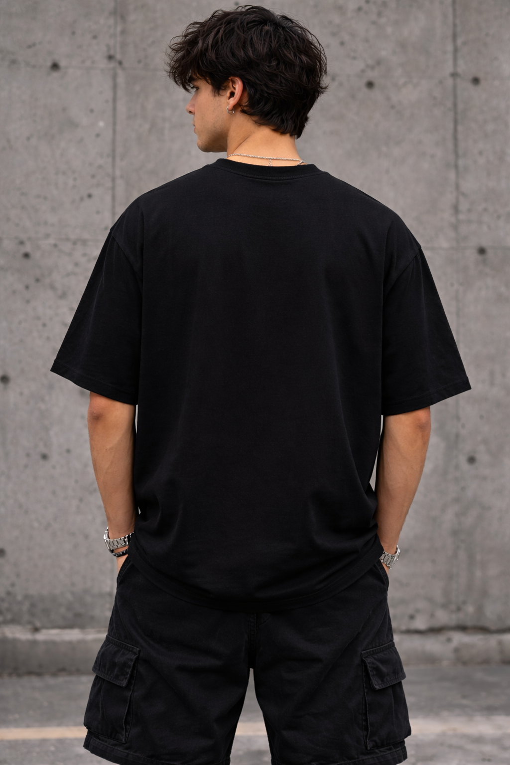 Person wearing a black t-shirt and cargo shorts standing against a concrete wall.