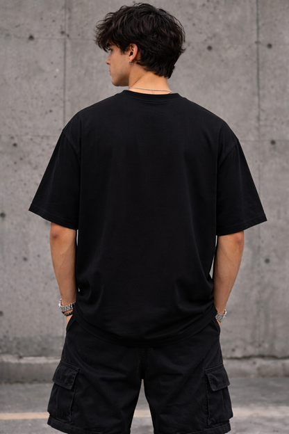 Person wearing a black t-shirt and cargo shorts standing against a concrete wall.
