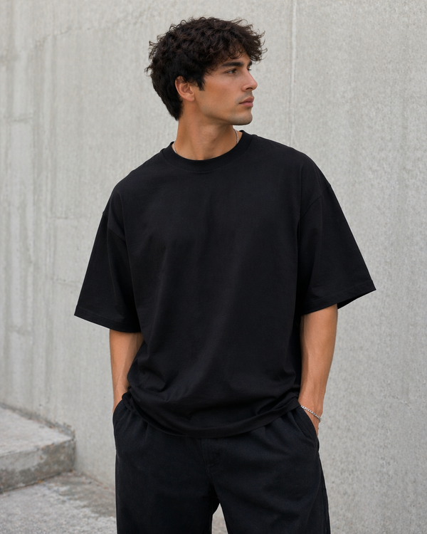 Man wearing a black t-shirt and pants against a gray concrete wall.