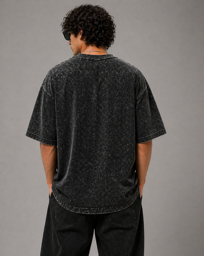 Person wearing a black acid-wash t-shirt against a gray background