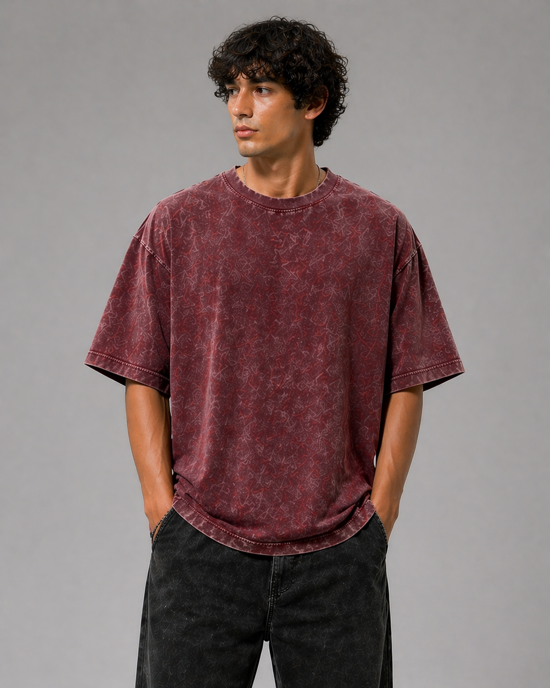 Man wearing a maroon t-shirt and black pants against a gray background