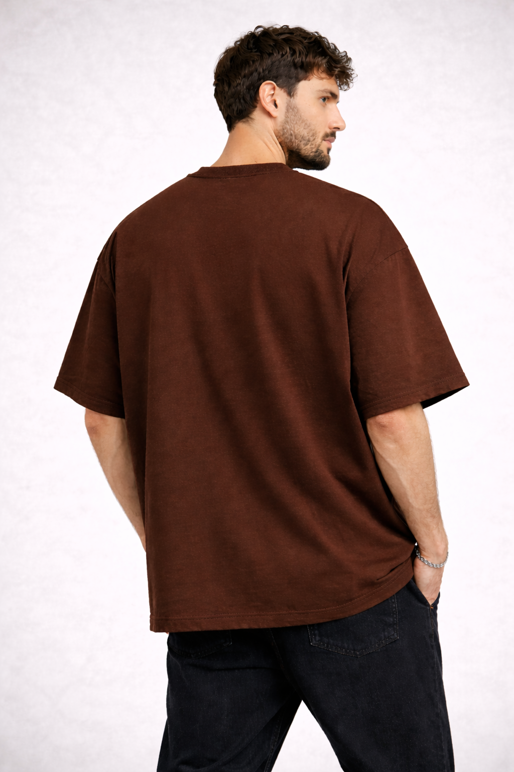 Man wearing a brown t-shirt and dark pants on a white background