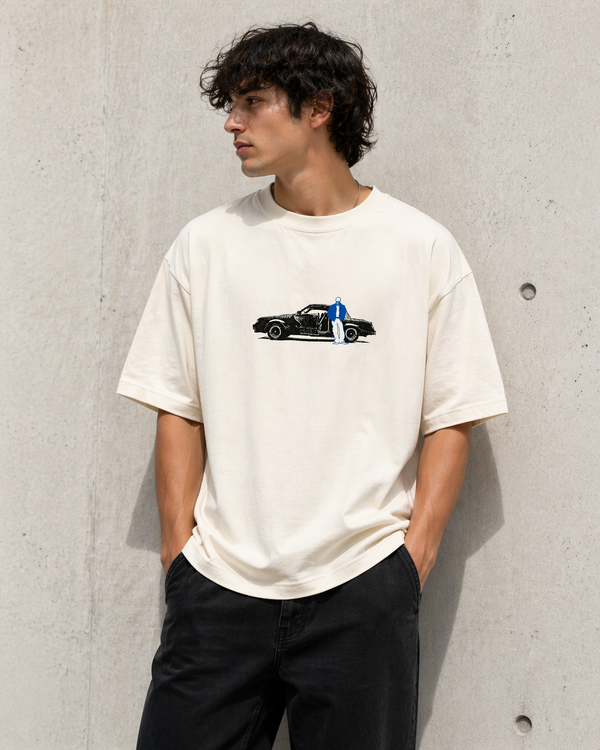 Person wearing a white t-shirt with a graphic design against a concrete wall.