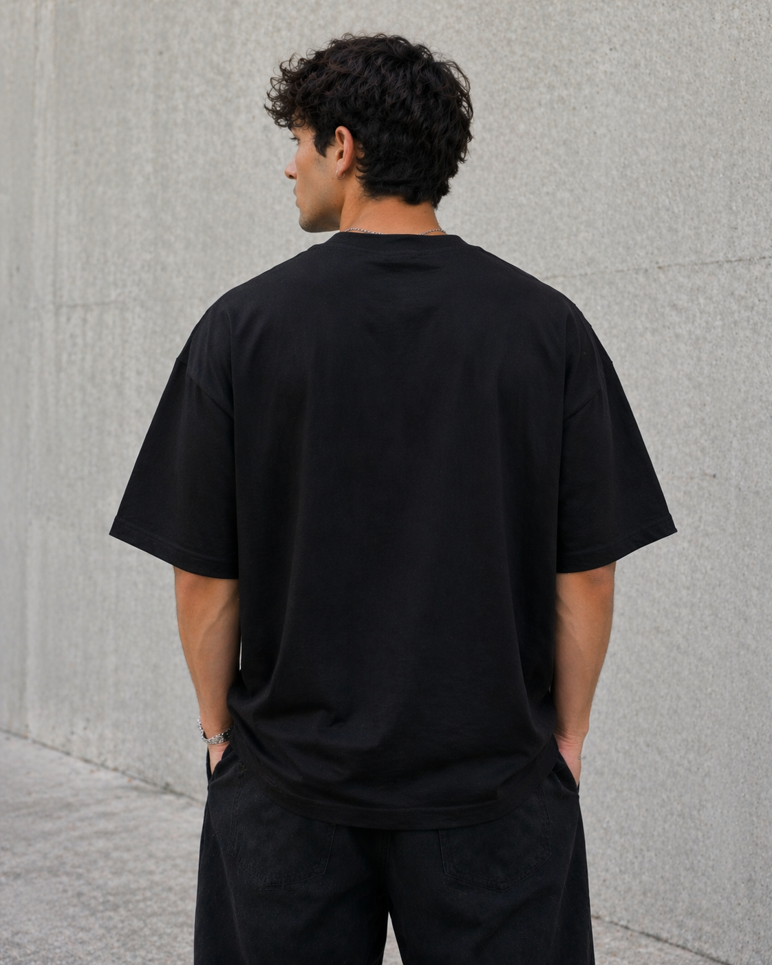 Man wearing a black t-shirt standing against a gray wall