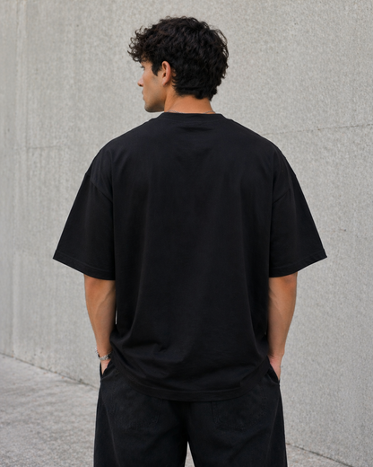 Man wearing a black t-shirt standing against a gray wall